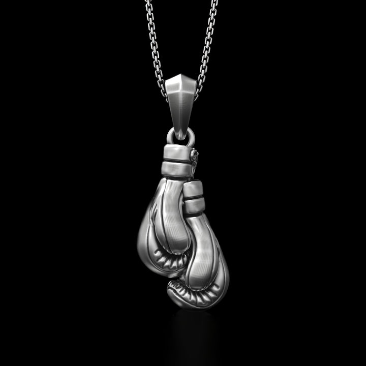 Silver boxing gloves pendant on a chain against a black background