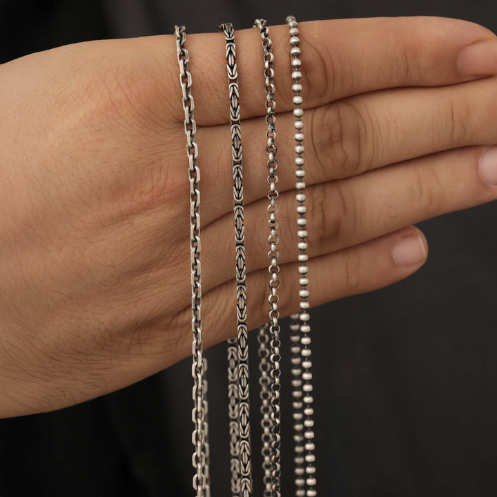 Three silver chains of different styles held in a hand against a dark background