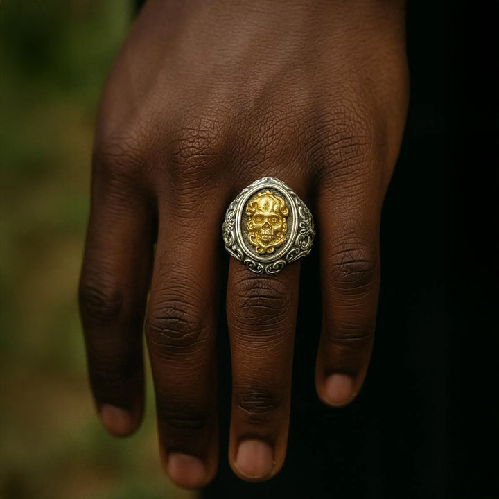 Vintage style silver skull ring on a person's finger with a blurred natural background