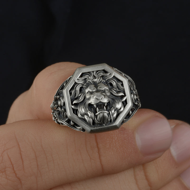 Silver lion head ring on a finger against a dark background
