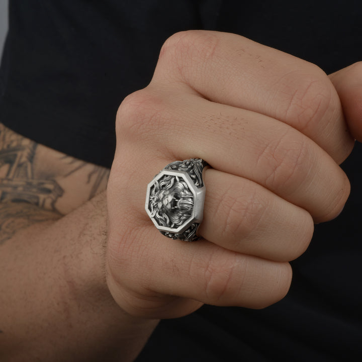 Close-up of a hand wearing a silver signet ring with intricate design on a dark background