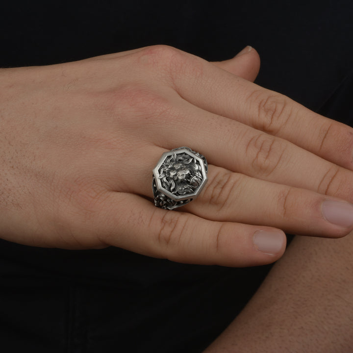 Hand wearing a statement signet ring with a detailed design on a black background