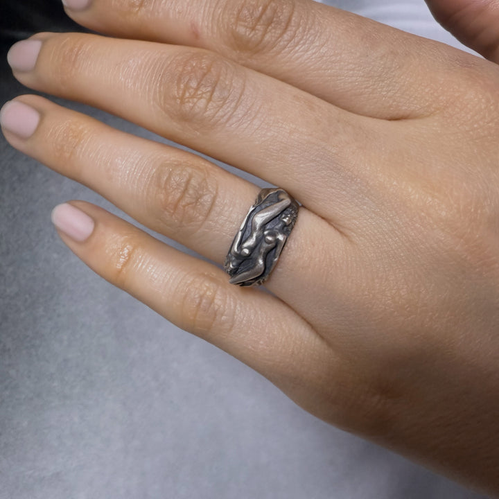 Hand wearing a silver ring with a detailed women couple symbol design on a neutral background