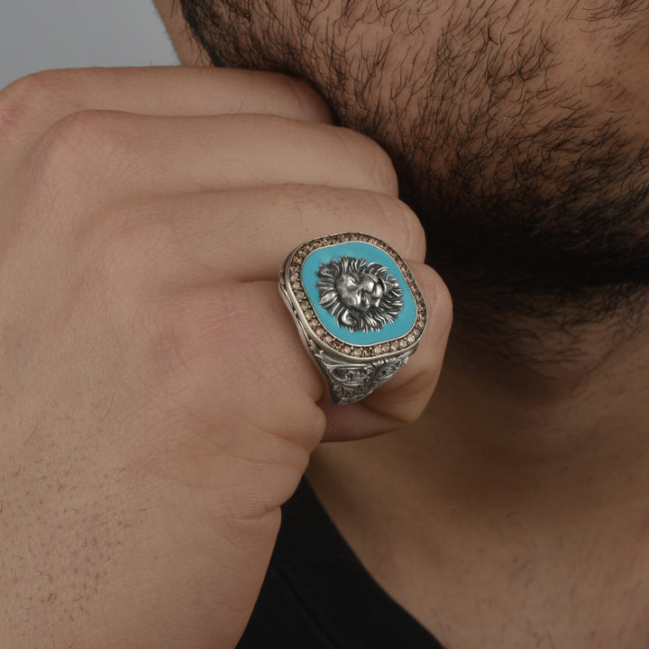 Close-up of a hand wearing a lion-themed ring with a blue turquoise center surrounded by zircon crystals.