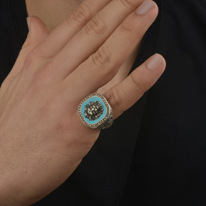 Hand wearing a ring with a blue turquoise stone and lion emblem on a black background