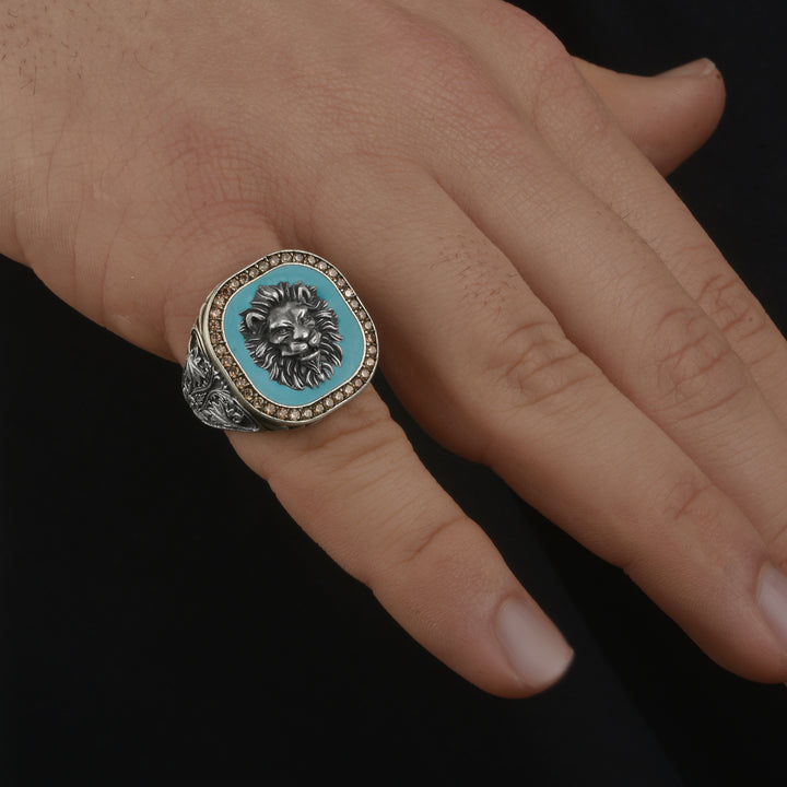 Silver ring with lion head emblem and blue center on a hand against a black background