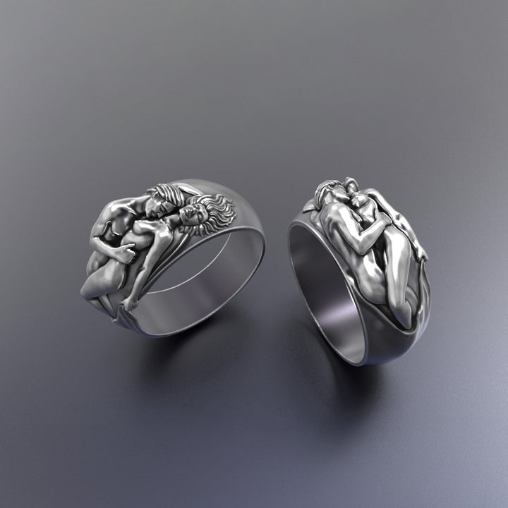 Two silver rings with artistic couple sculpture designs on a gray background