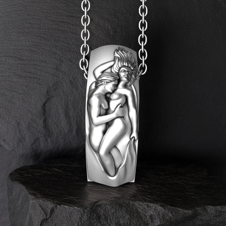 Silver pendant with a design of two lovers embracing on a dark stone surface.