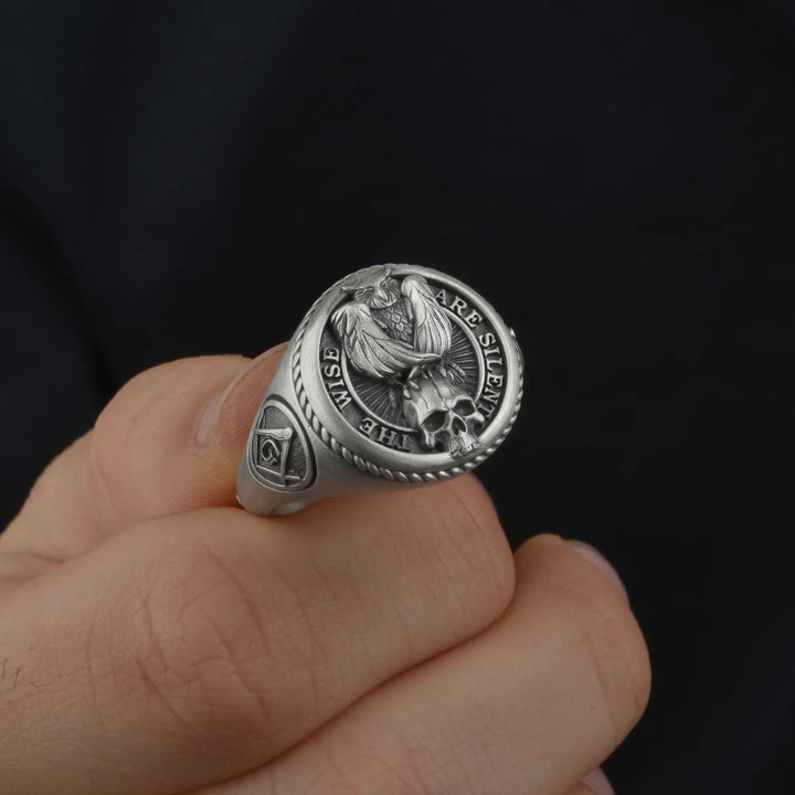 Silver masonic owl ring with intricate design held by a hand against a dark background