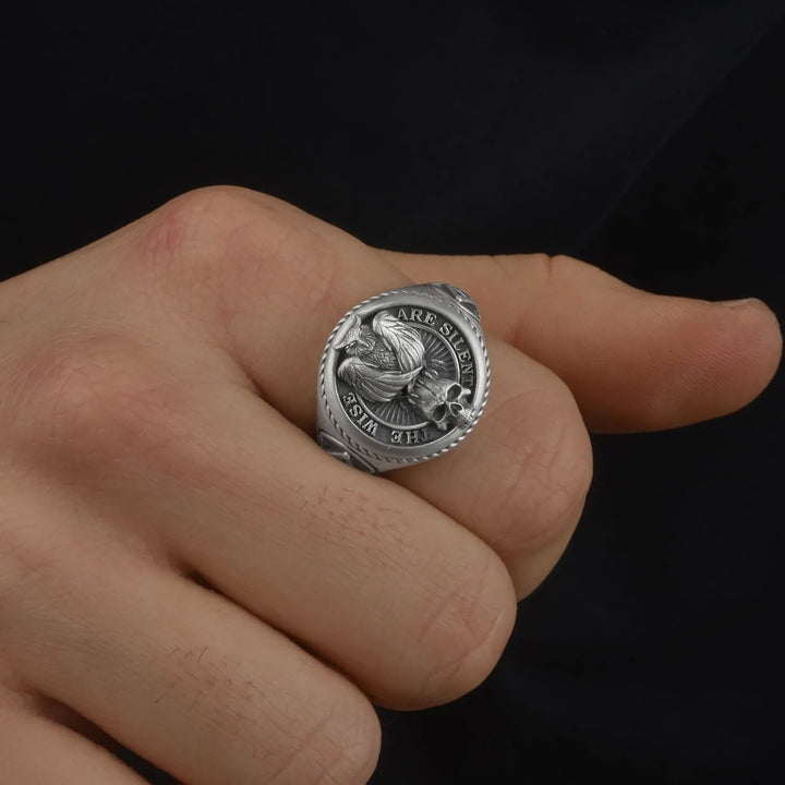 Silver masonic owl ring with engraved “The Wise Are Silent” quote on a person's finger against a black background