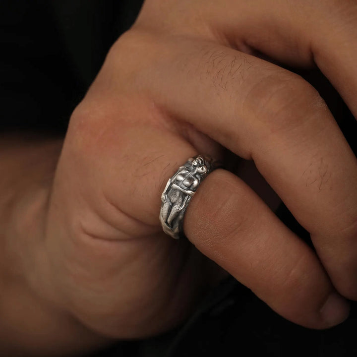 Silver band ring with a detailed couple embrace design on a person's finger against a dark background