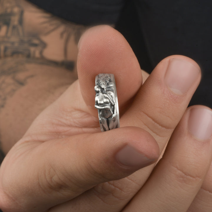 Close-up of a hand holding an artistic silver ring with a detailed lovers embrace design.