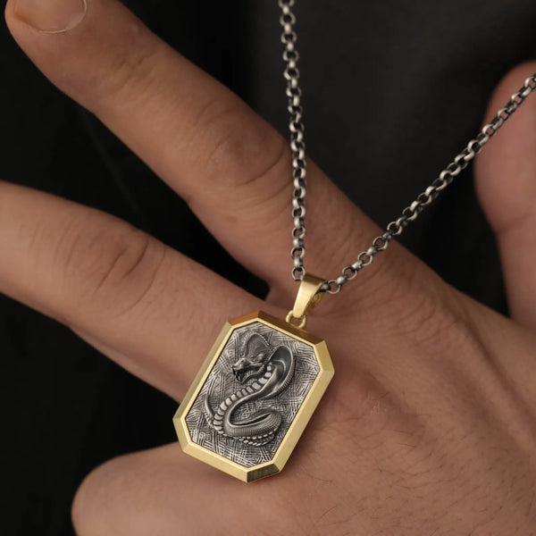 Gold and silver pendant with snake design held in a hand against a dark background