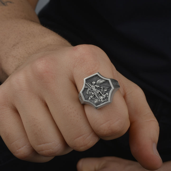 Close-up of a hand wearing a detailed silver ring with a christian religiuos motif on a dark background