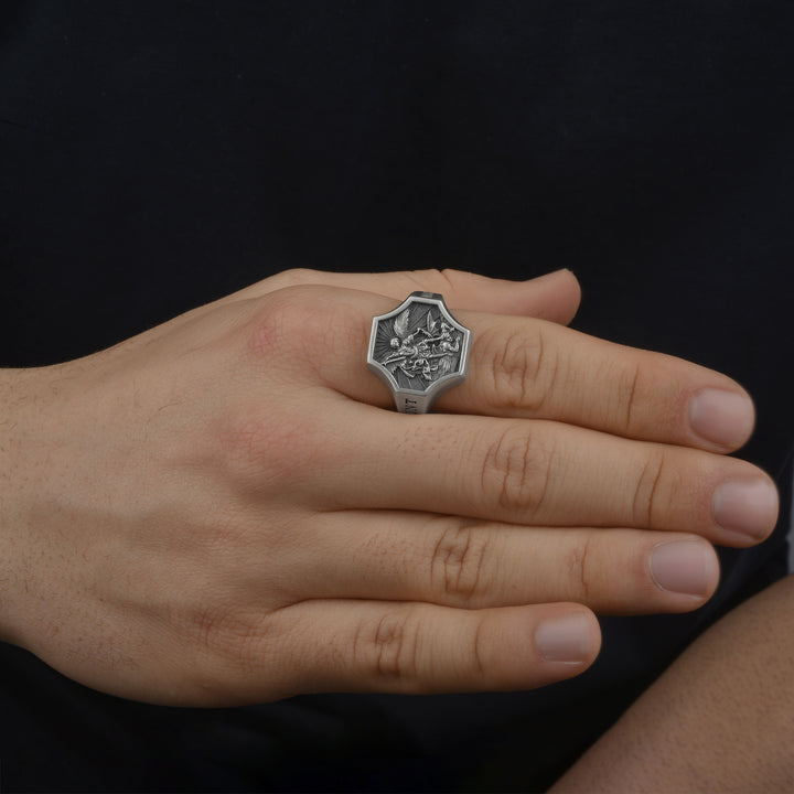 Hand wearing a silver ring with an intricate catholic religious design on a black background