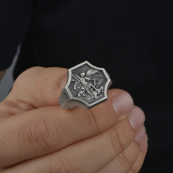 Silver ring with detailed st Michael archangel design held in a hand against a dark background